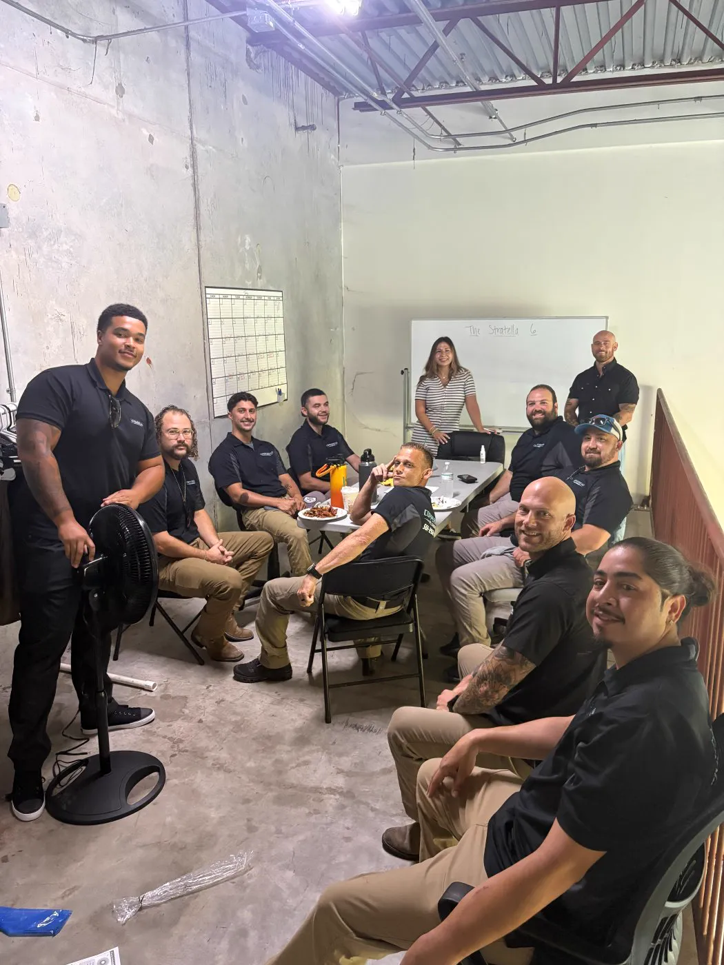 A team in dark uniforms gathered on a shop floor for training