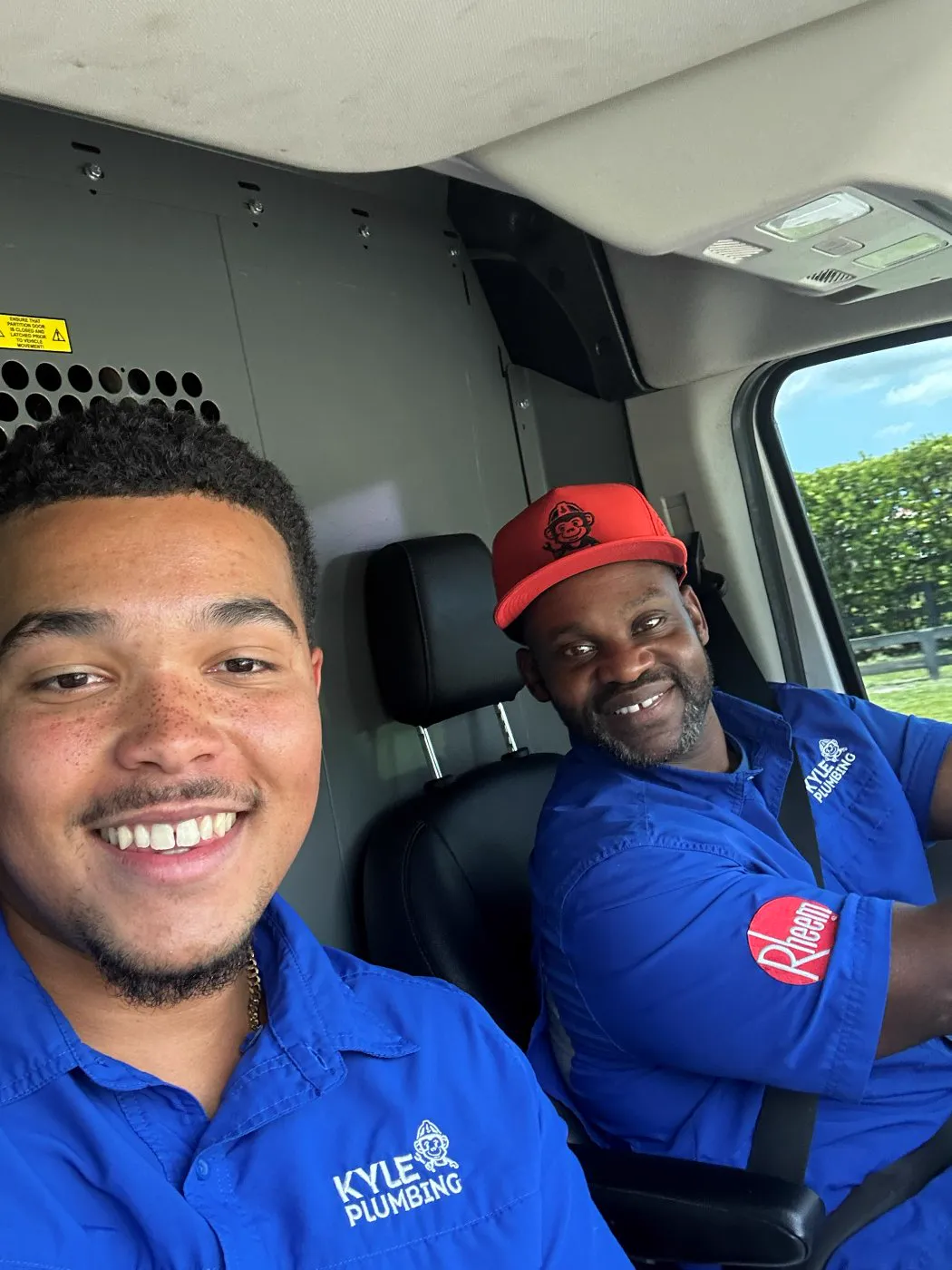 Two plumbing technicians smiling in the cab of a service van